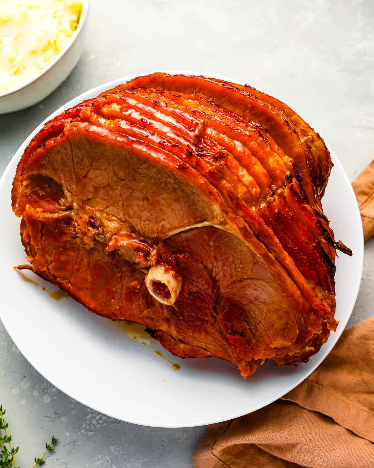 A crockpot spiral ham on a plate next to a bowl of mashed potatoes.