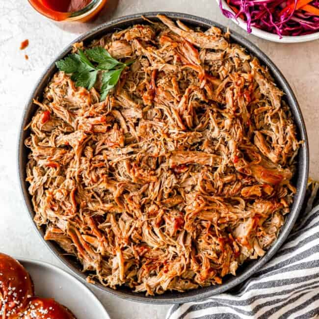 Pulled pork on a plate next to a bowl of coleslaw.