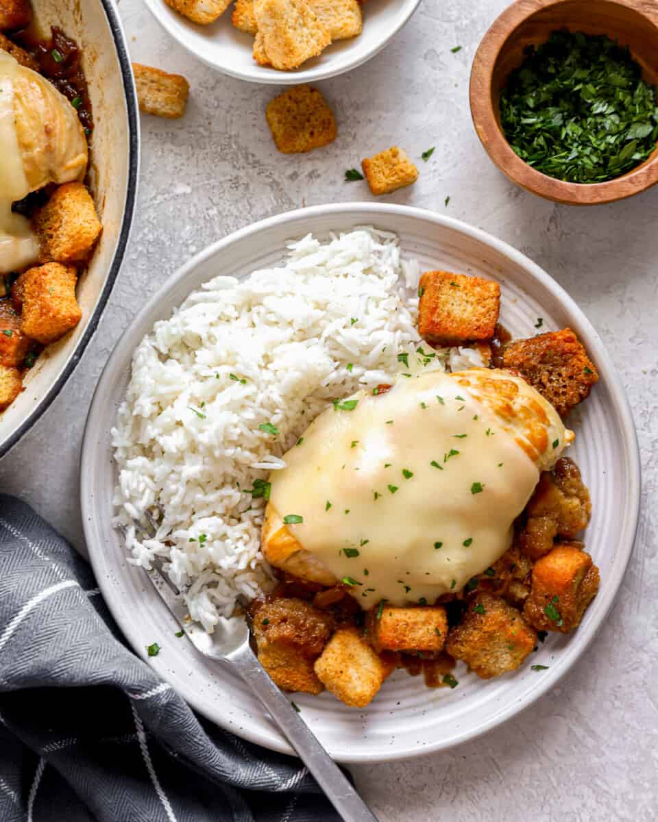 A white plate with French onion chicken and rice on it.