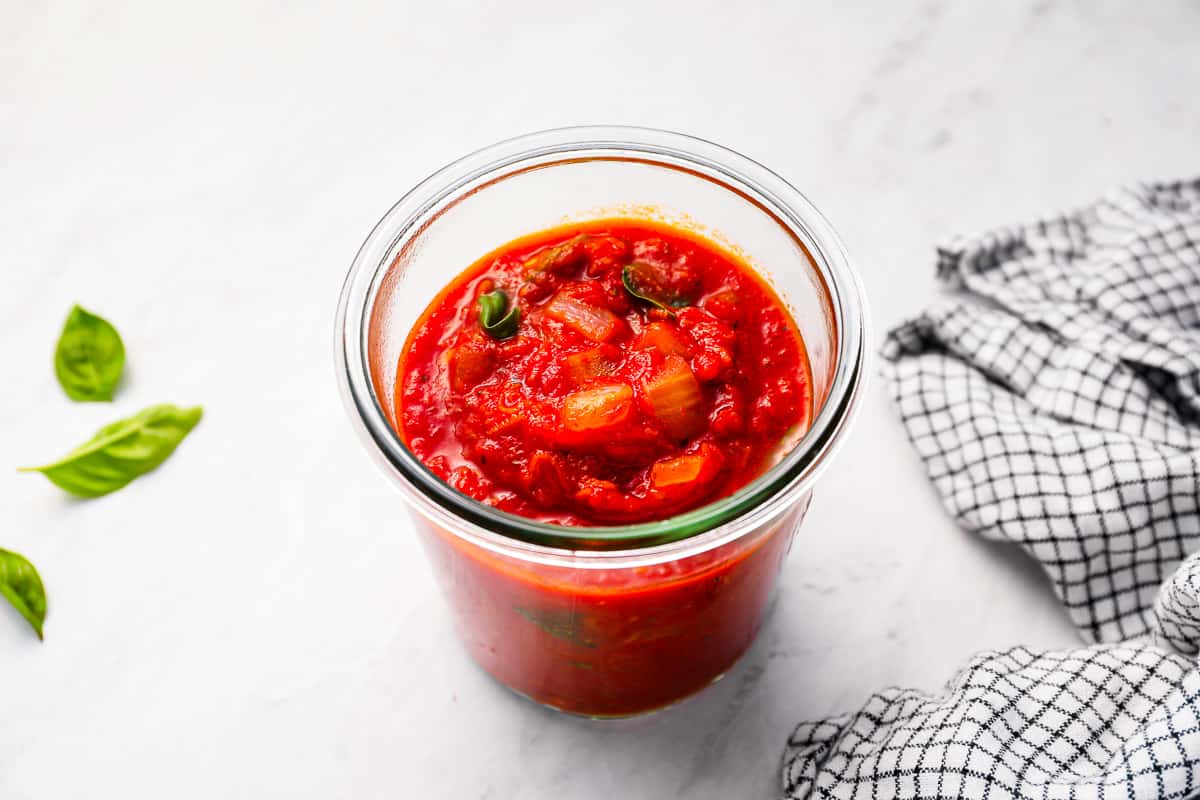 Homemade spaghetti sauce in a glass on a marble table.