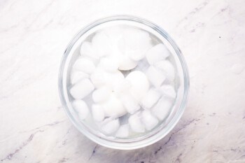 Ice cubes in a glass bowl on a marble surface.