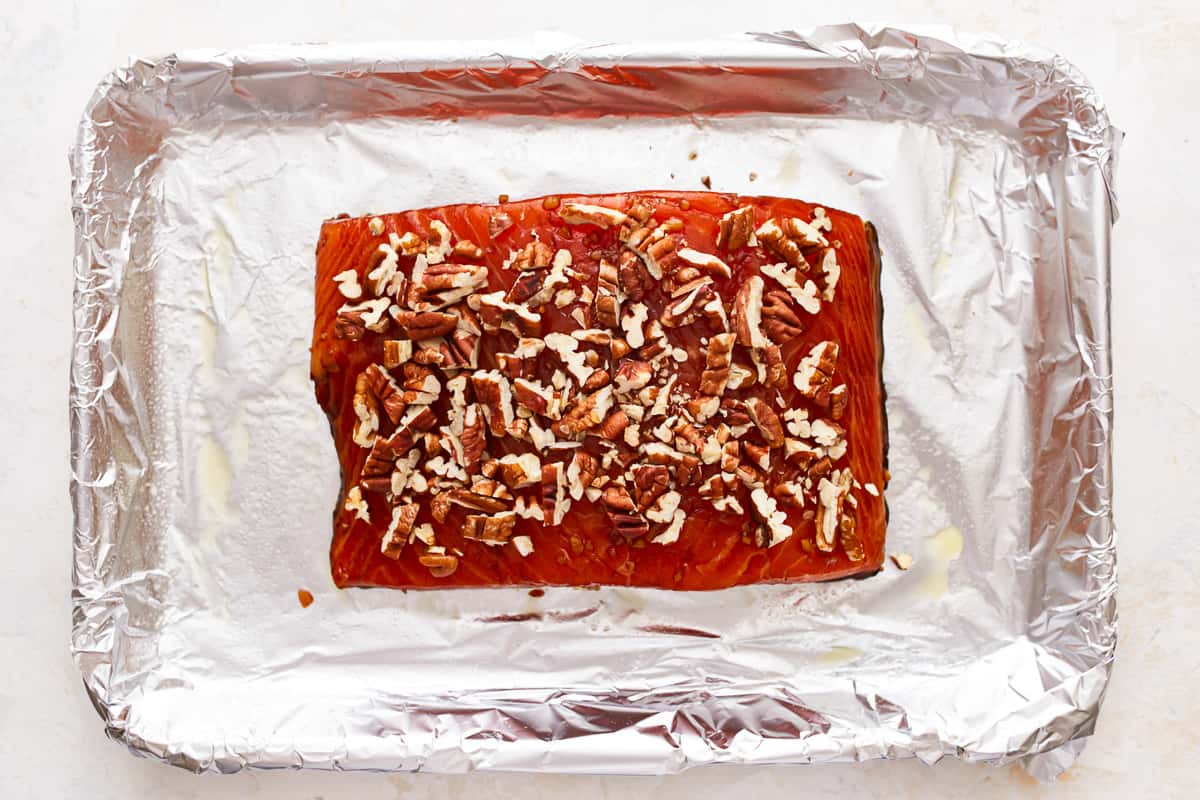 a salmon filet topped with pecans on a baking sheet.