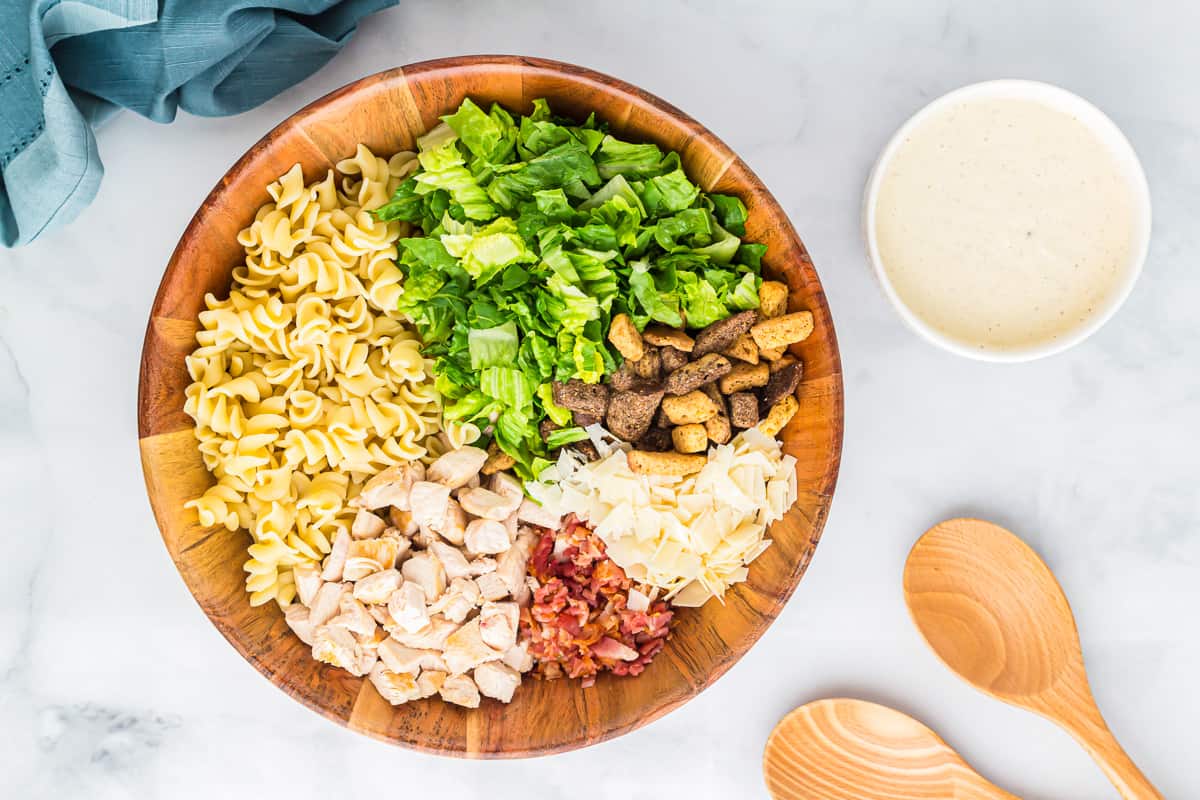 A wooden bowl filled with pasta, salad, and dressing.