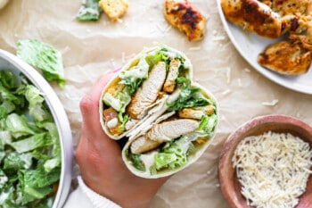 A person is holding a chicken burrito and salad.