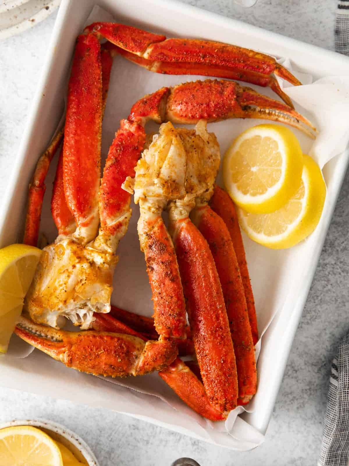 overhead view of 2 clusters of snow crab legs and lemon slices on an askew white rectangular plate.