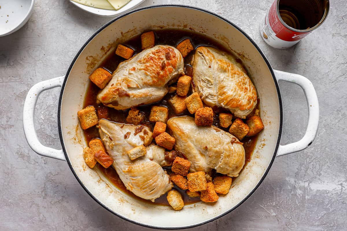 Chicken breasts in a pan with French onion soup and croutons.