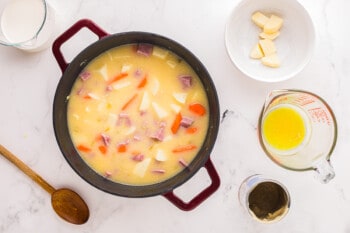 A pot of soup with carrots, potatoes and ham.