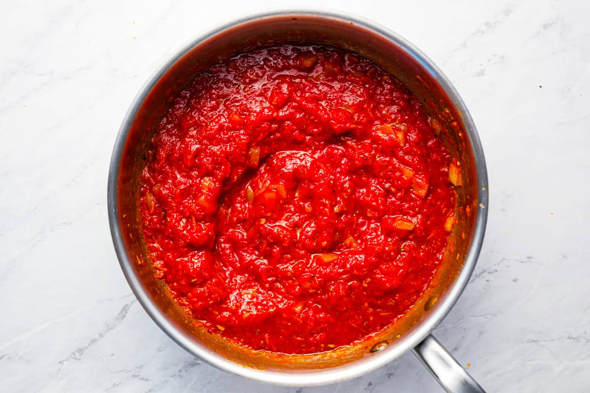 Red sauce in a pan on a marble countertop.