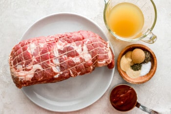 A piece of meat on a plate next to a bowl of sauce.