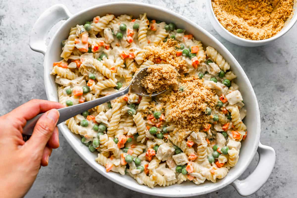 A person taking a spoonful of chicken pasta in a white dish.