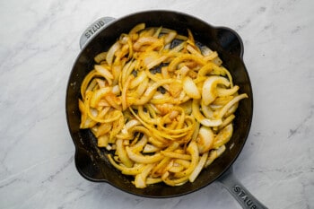 Fried onions in a skillet on a marble countertop.