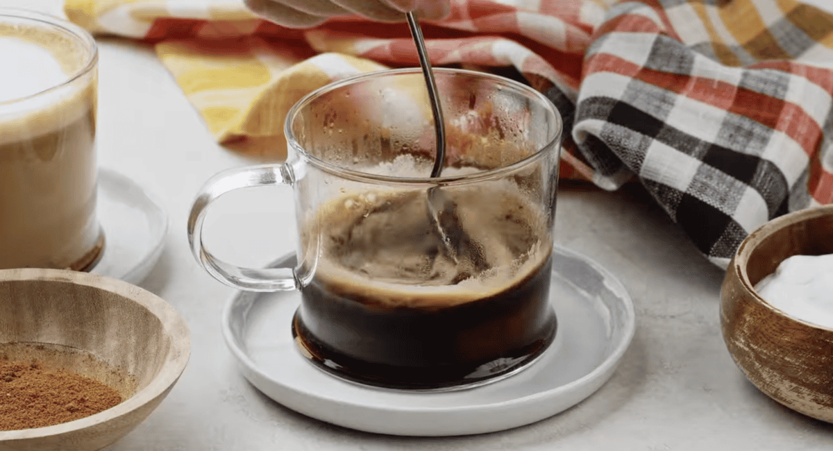 stirring pumpkin puree into a cup of espresso with a spoon.