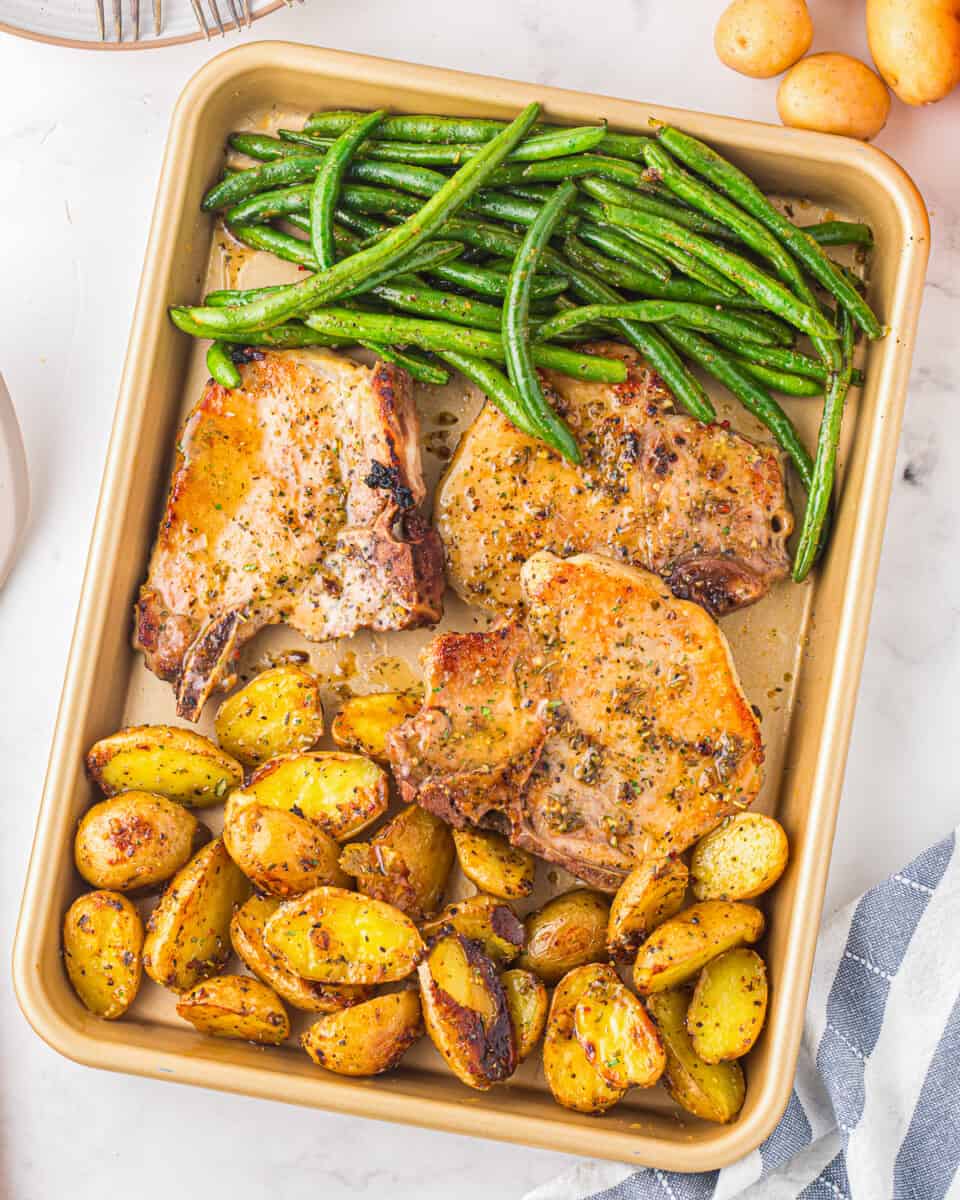 A baking sheet pan with pork chops, potatoes, and green beans.