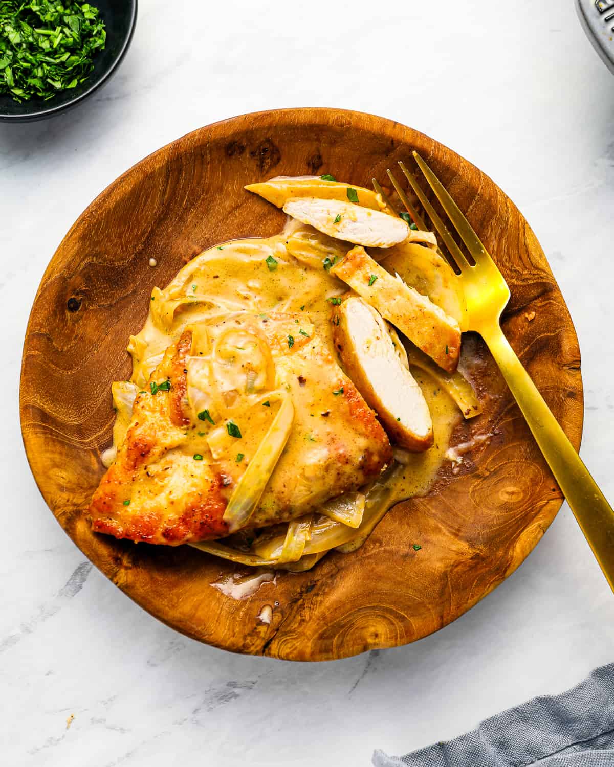 a plate of smothered chicken, partially cut into slices, with large sliced of onion.