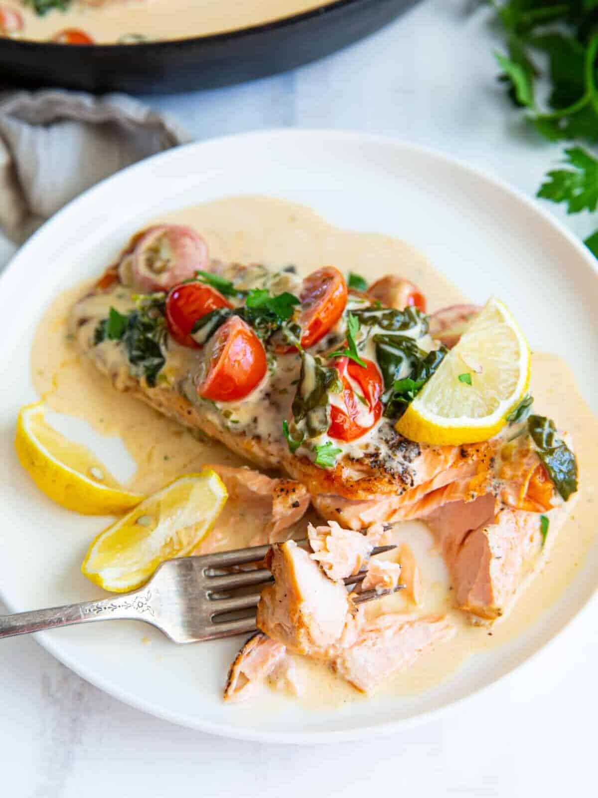 three-quarters view of a partially eaten filet of creamy tuscan salmon on a white plate with a fork.