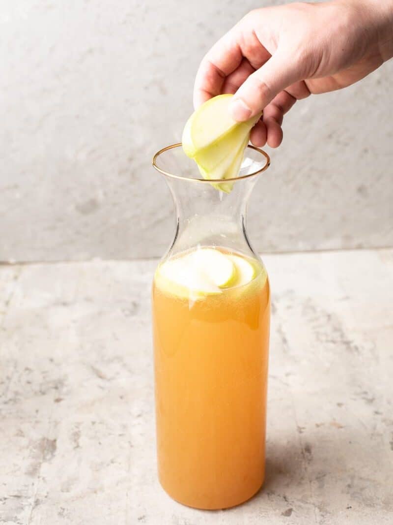 A person pouring an apple cider into a pitcher, creating a delicious apple pie drink.