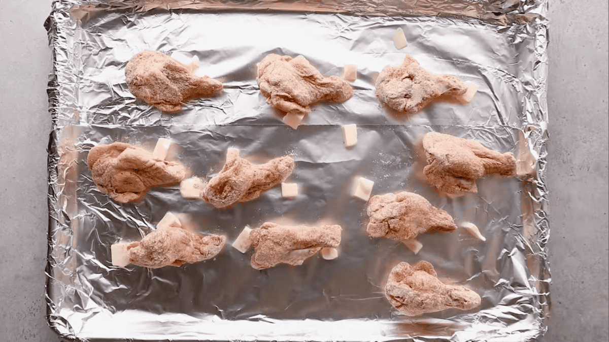 seasoned chicken wingettes spread out on a foil lined baking sheet dotted with butter.