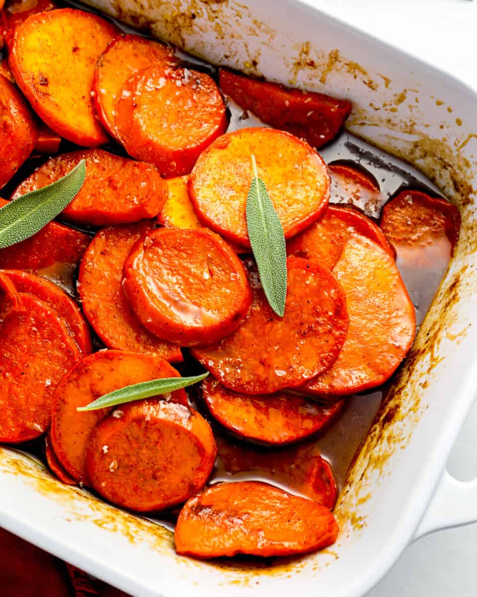 A white baking dish filled with candied yams and sage.