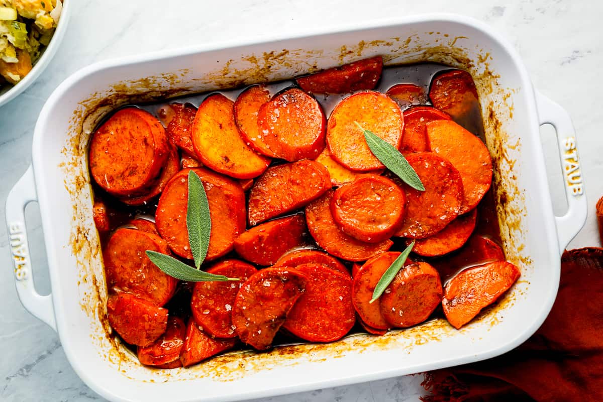 Candied sweet potato yams in a white dish with sage.