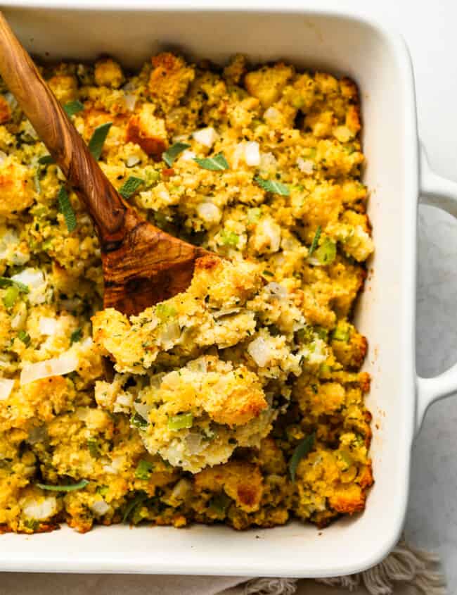 Cornbread stuffing in a white dish with a wooden spoon.