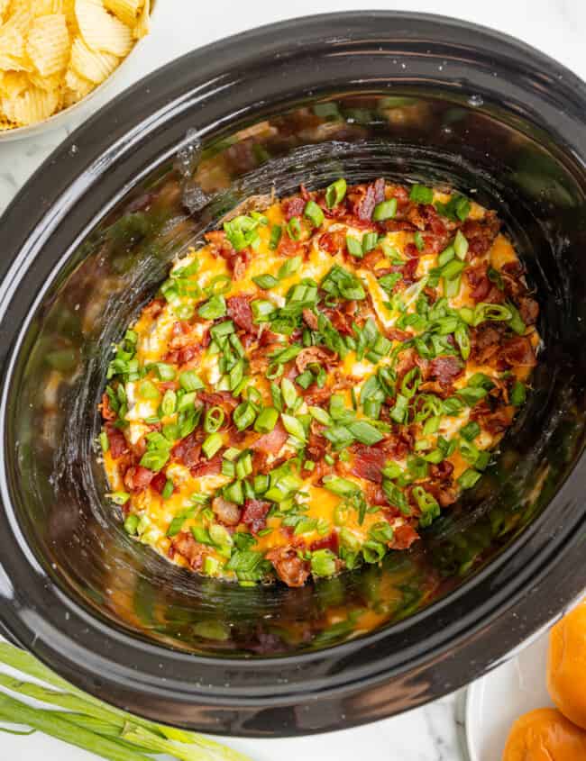 A crock pot filled with bacon and green onions.