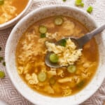 A bowl of asian chicken soup with a spoon.