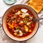 A bowl of soup with meat, vegetables and bread.