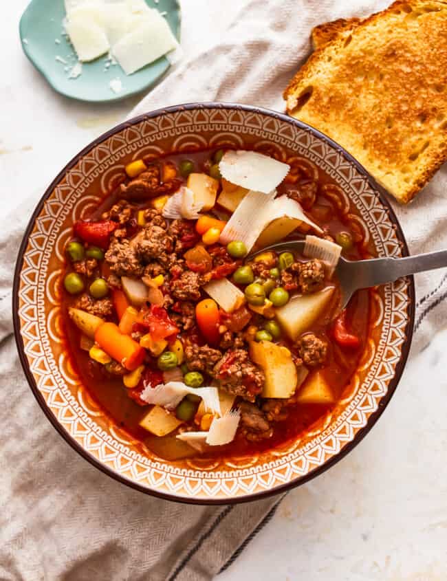 A bowl of soup with meat, vegetables and bread.