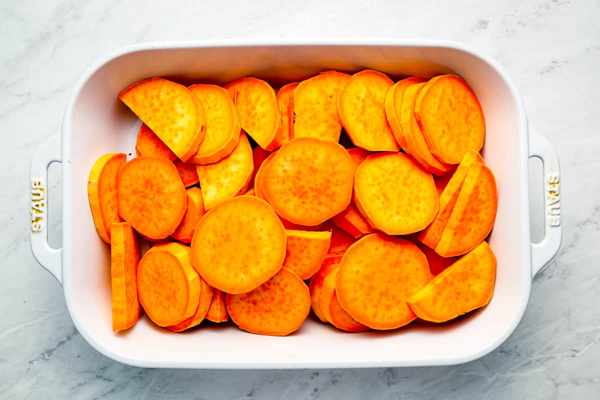 Sliced sweet potatoes in a white baking dish.