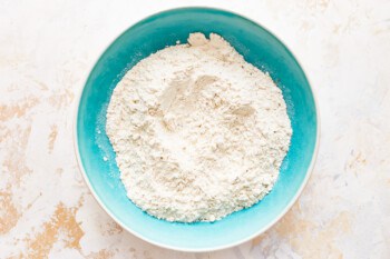 Flour in a blue bowl on a marble surface.