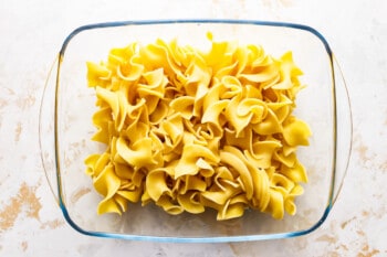 Penne pasta in a glass bowl on a marble surface.