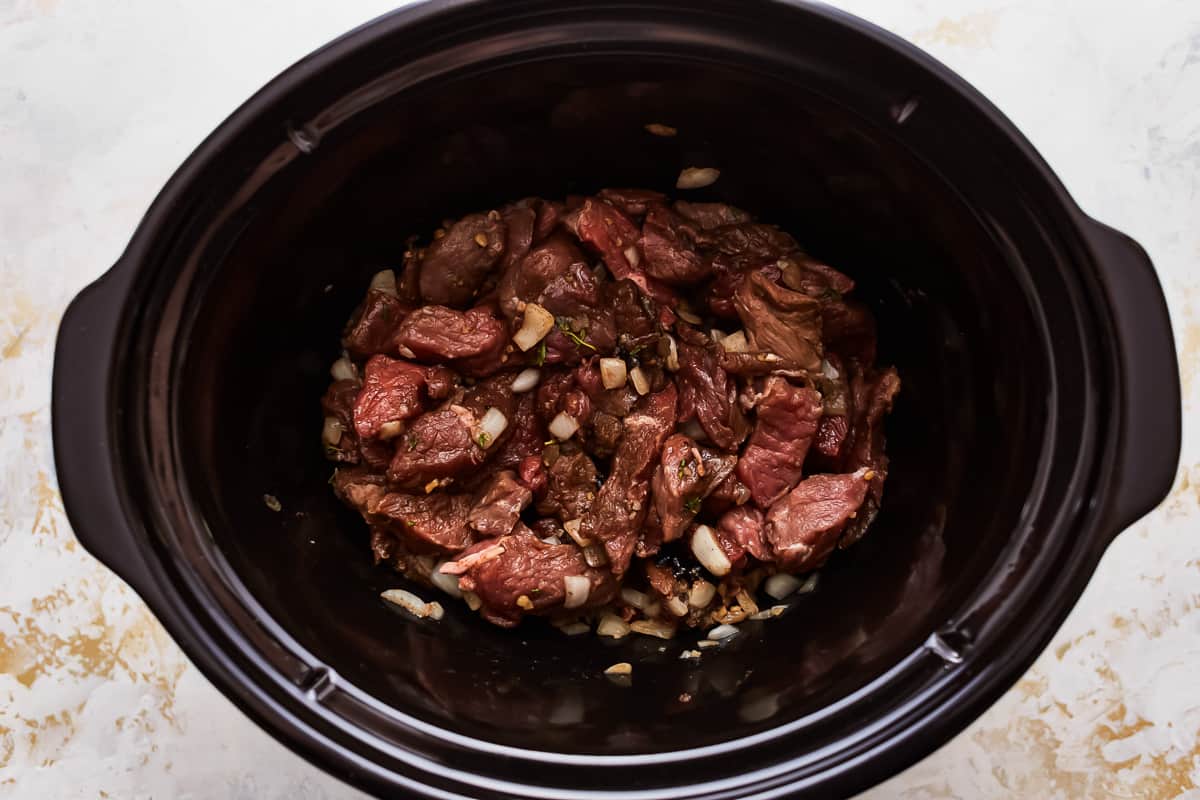 A crock pot filled with beef and onions.