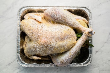 A turkey in a foil container on a marble countertop.