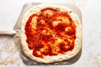 A pizza with sauce and cheese on a baking sheet.