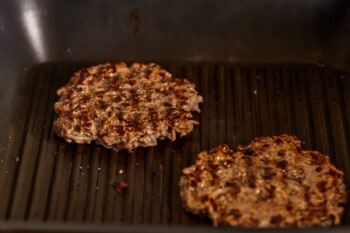 Two hamburger patties are being cooked in a pan.