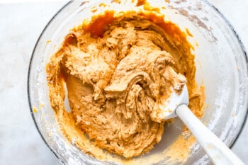 A bowl of pumpkin batter with a spoon in it.