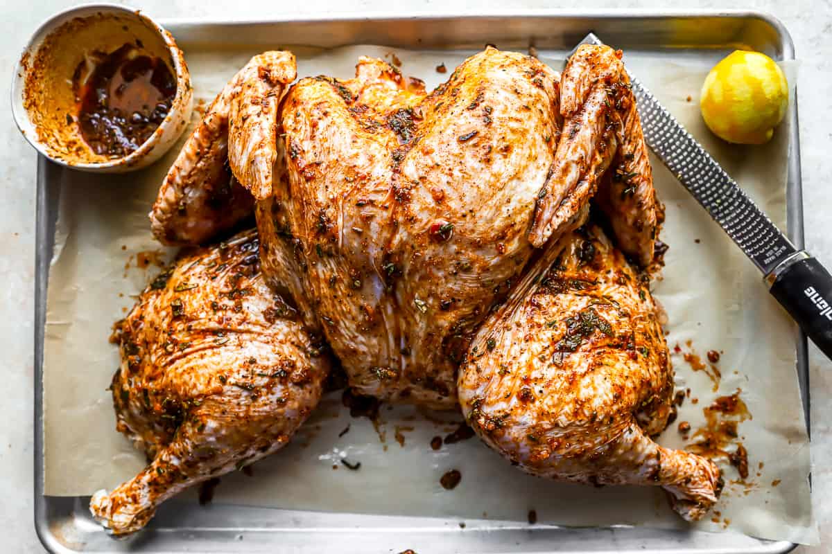 A roasted chicken on a baking sheet with lemons and a knife.