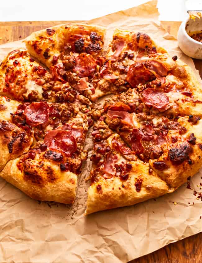 A cut meat lovers pizza on parchment paper.