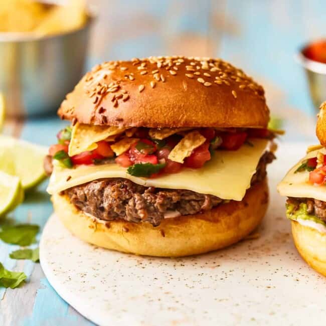 Two burgers on a plate with chips and salsa.