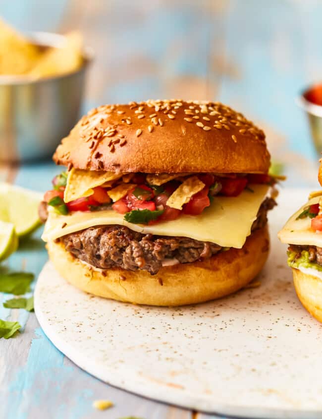 Two burgers on a plate with chips and salsa.