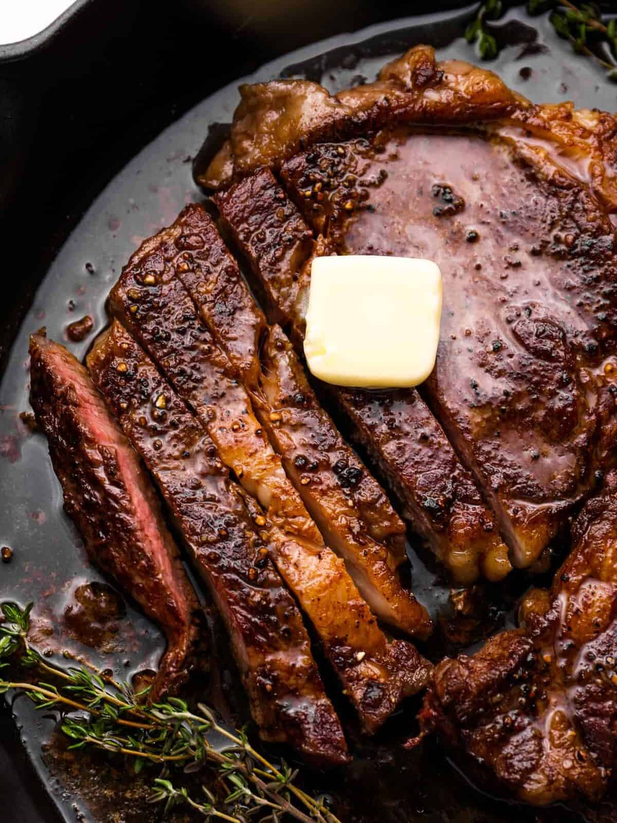 close up of partially sliced oven cooked steak with a pat of butter on top in a cast iron pan.