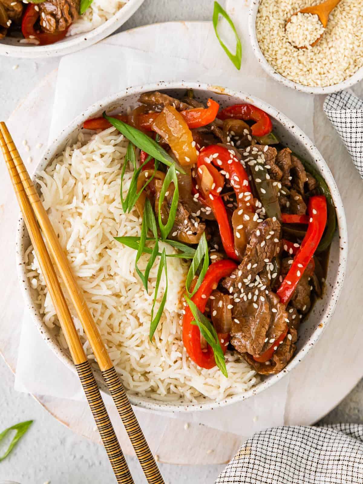 a bowl of pepper steak stir fry with rice and chopsticks.