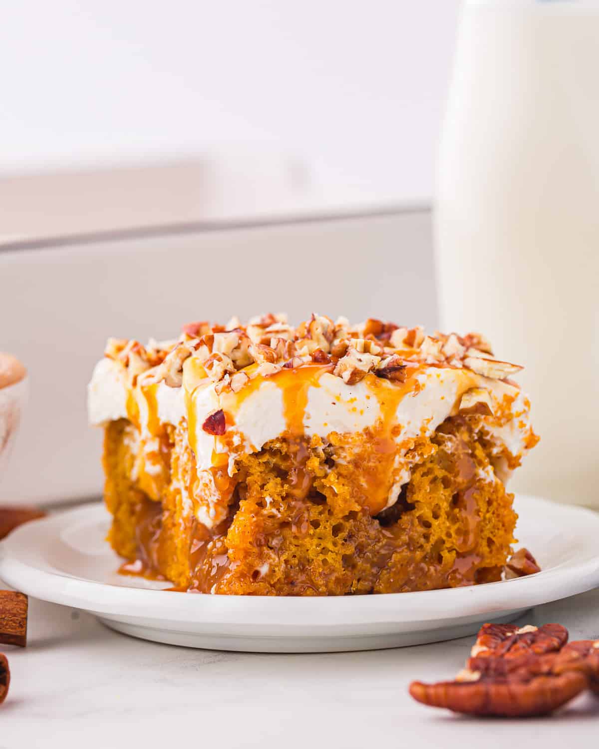 A slice of pumpkin caramel poke cake on a plate, next to a glass of milk.