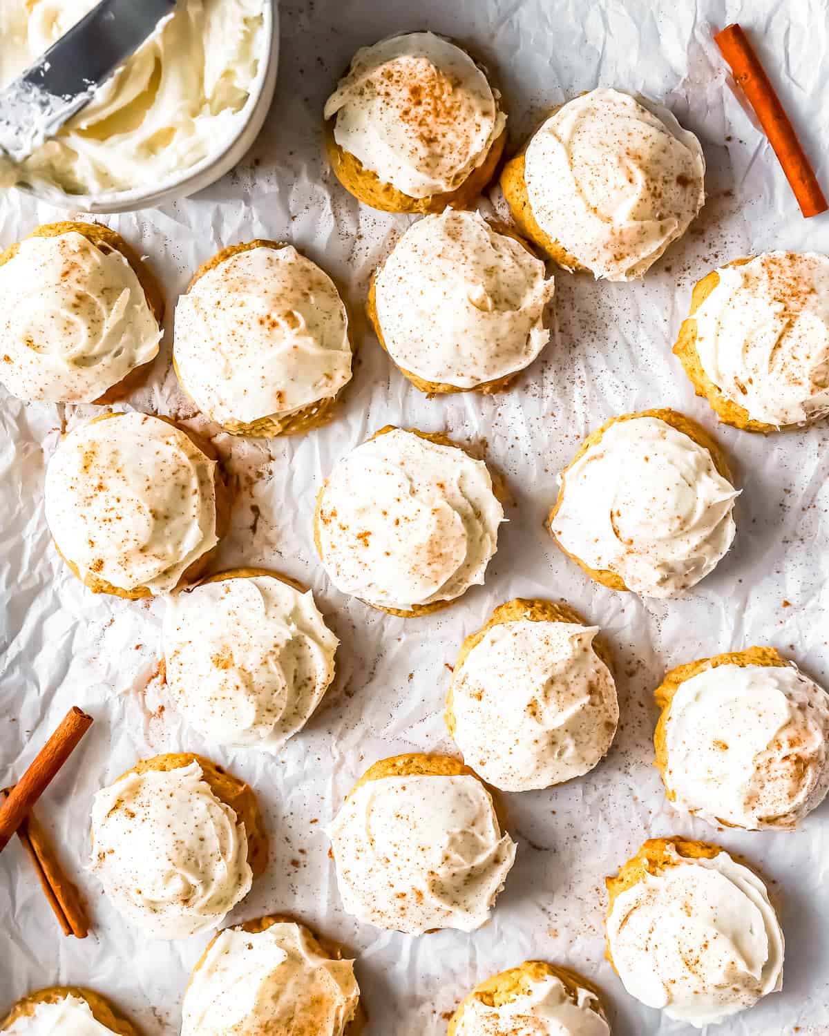 Frosted pumpkin cookies on a baking sheet with icing and cinnamon sticks.