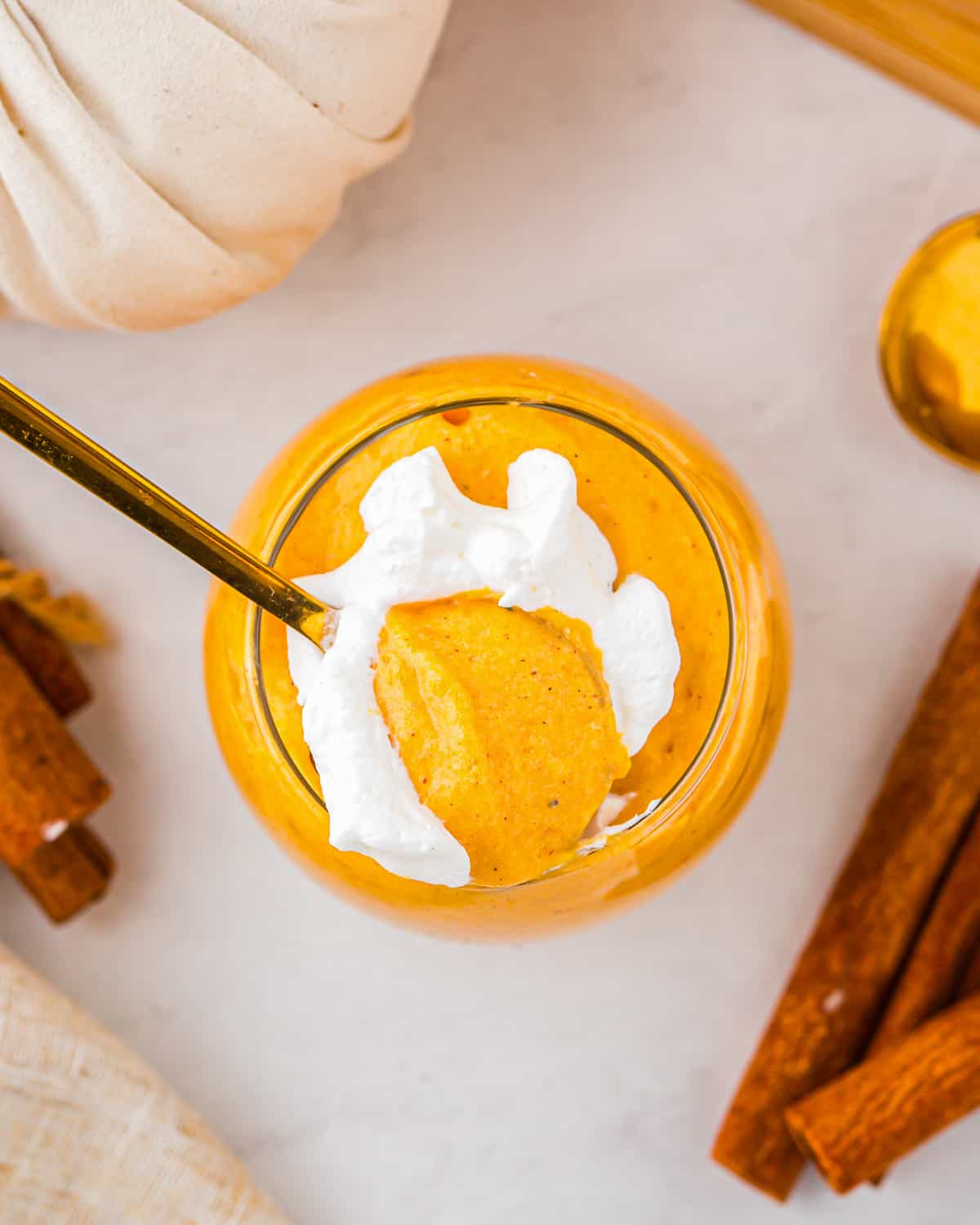 A glass of pumpkin mousse with whipped cream and cinnamon sticks.