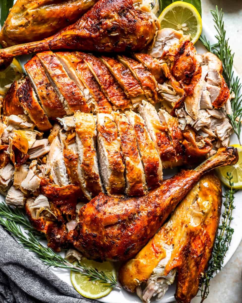 Roasted turkey on a white plate with lemons and rosemary.