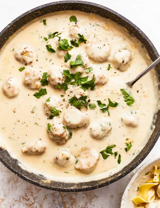 A bowl of pasta with meatballs and parsley.