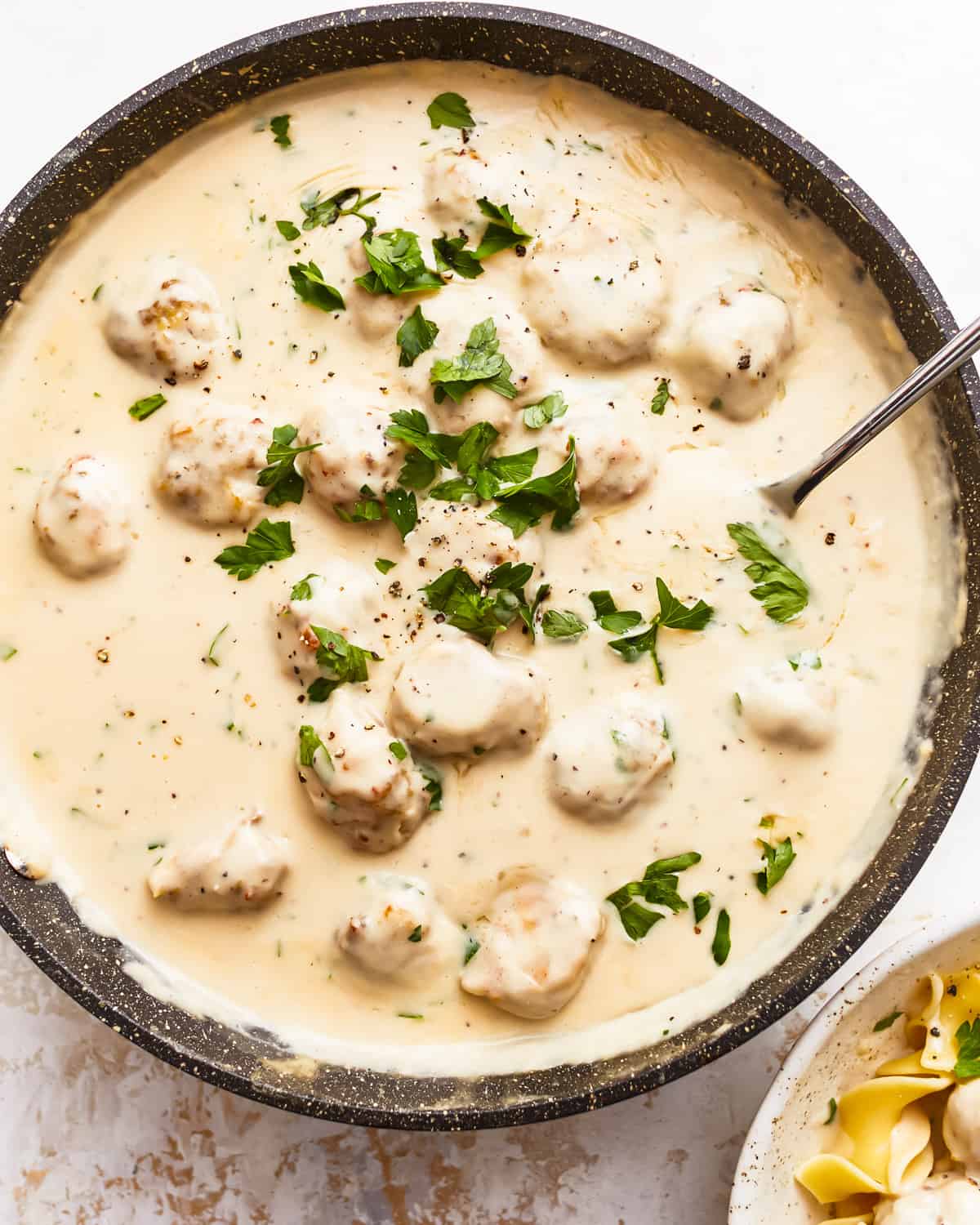 A bowl of pasta with meatballs and parsley.