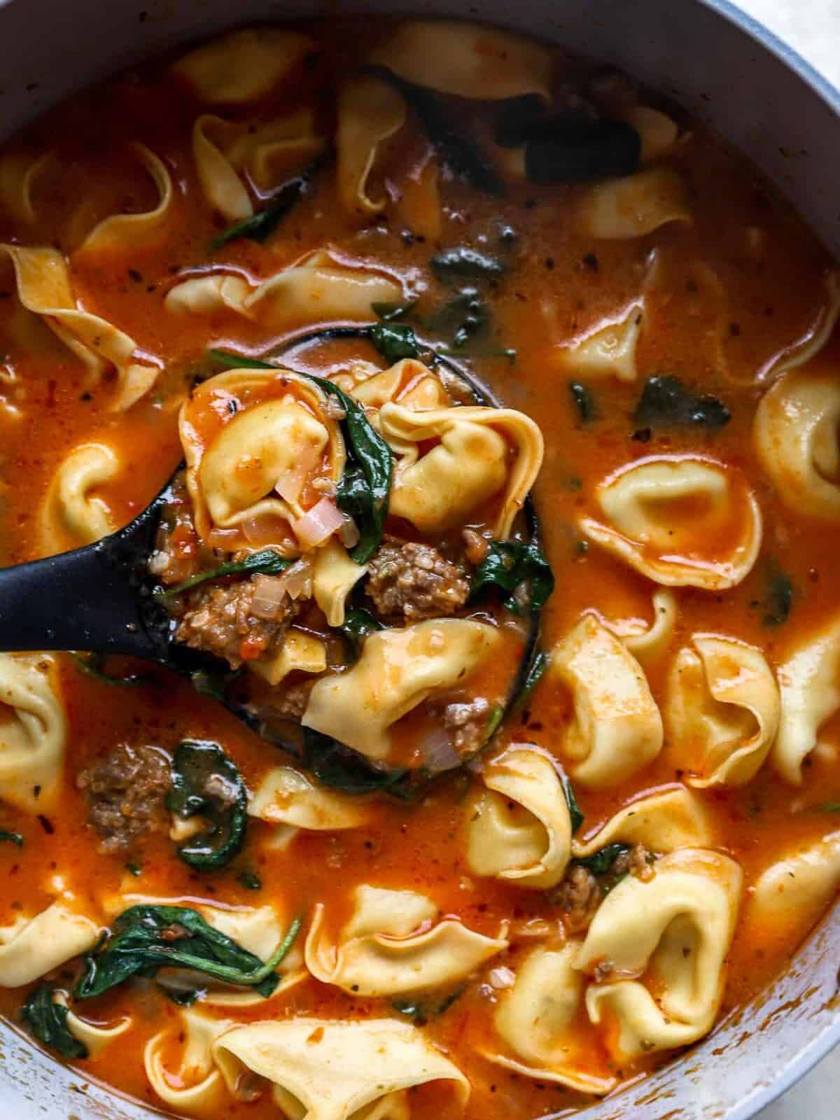 close up view of a ladle scooping up tortellini soup from a pot.