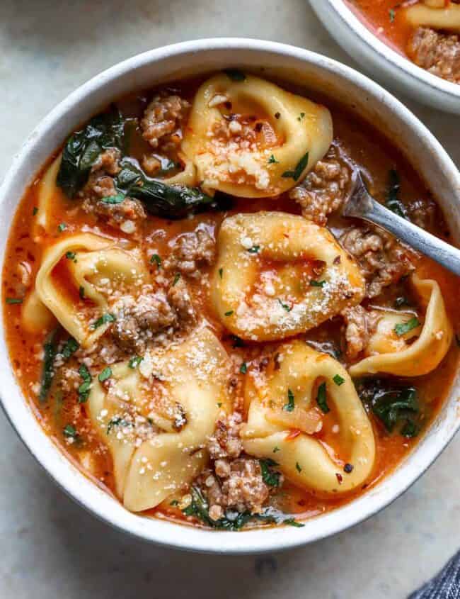 overhead view of tortellini soup in a white bowl with a spoon.